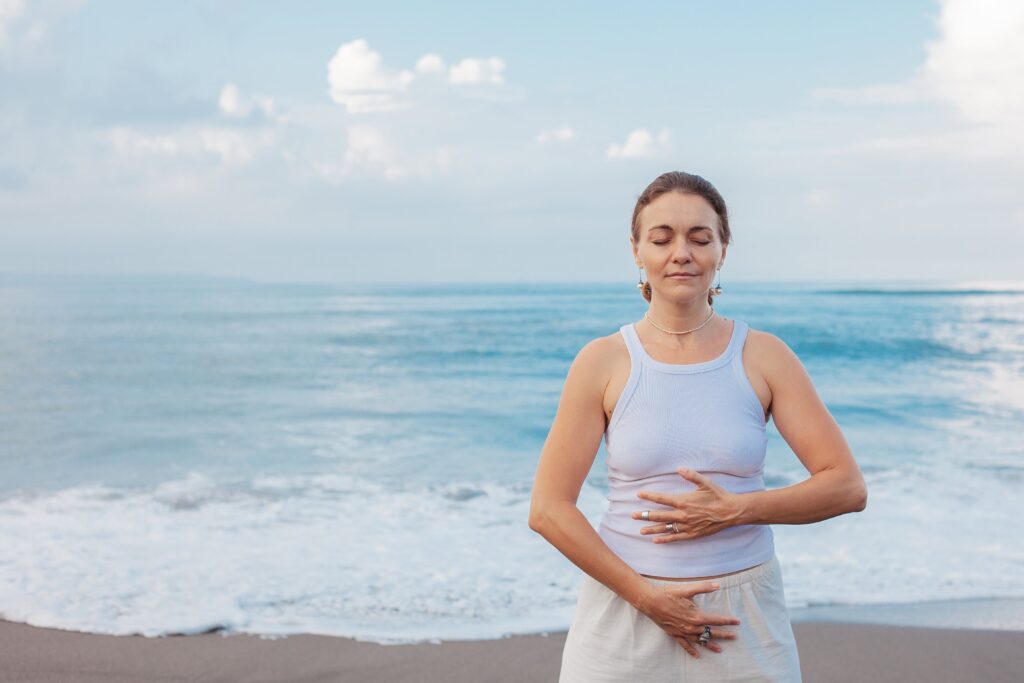 a woman standing on a beach with her hands on her stomach - Qigong practices