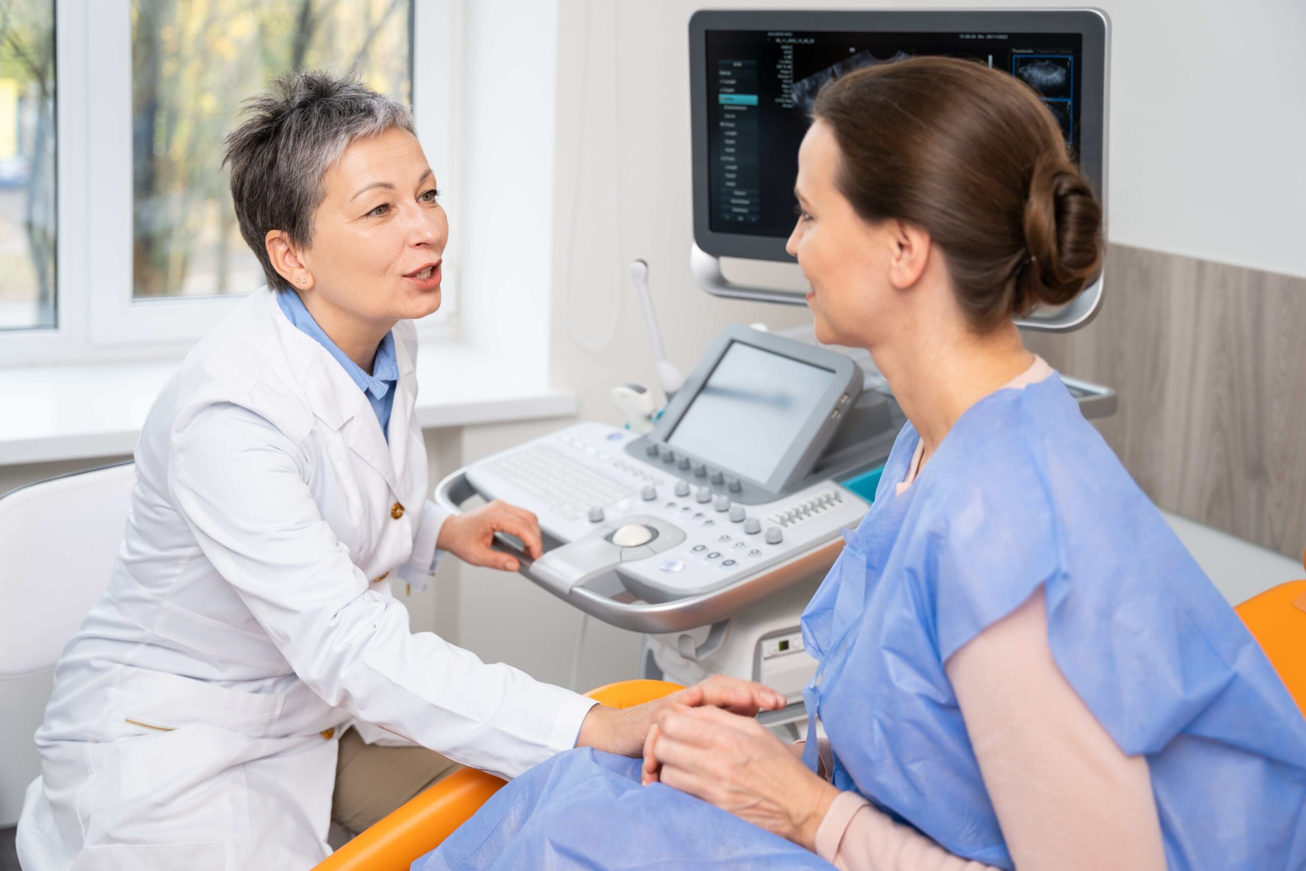 A healthcare professional speaks with a patient about hormonal health and fertility, with an ultrasound machine in the background.