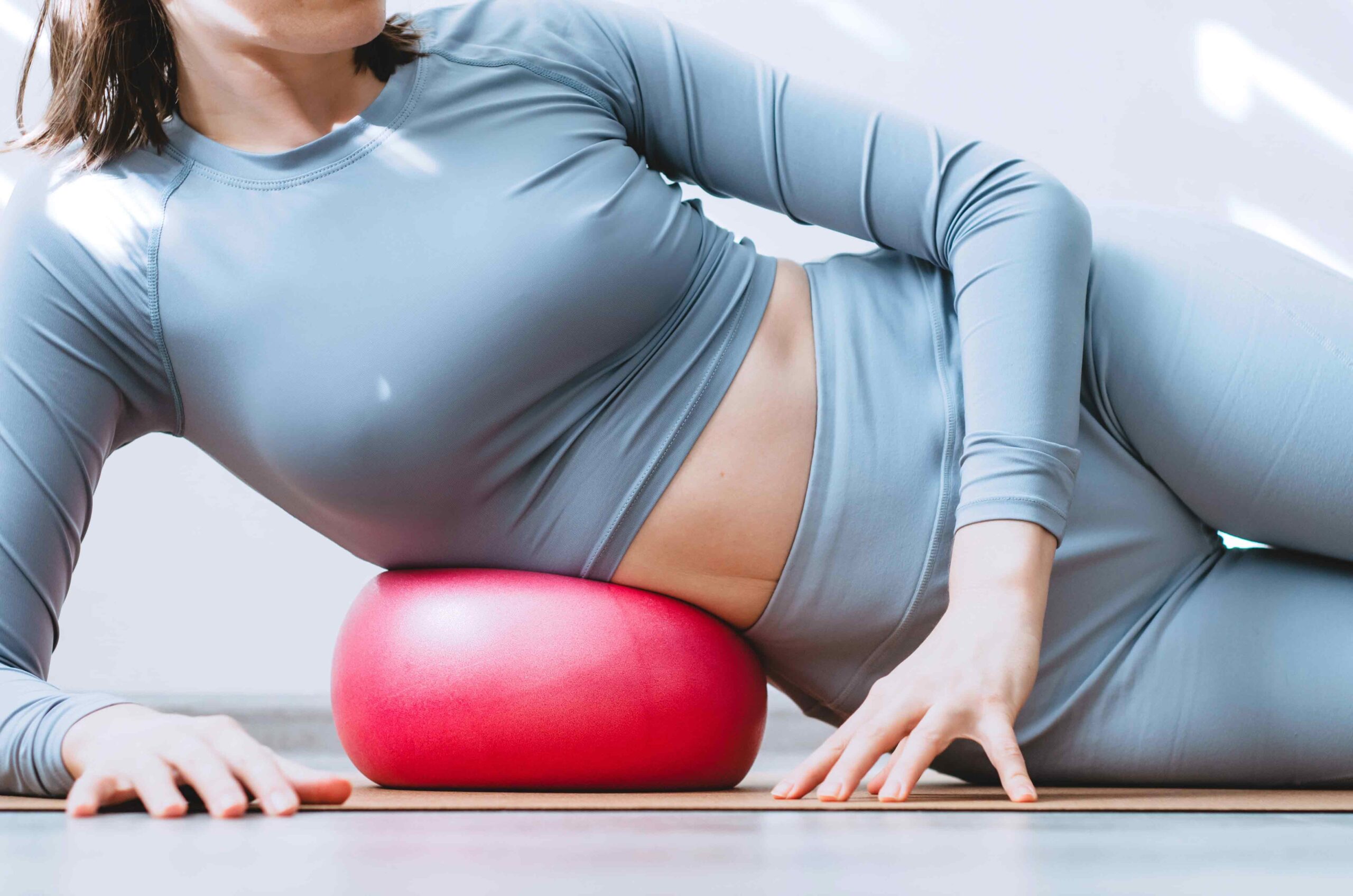 Woman practicing yoga for anxiety relief, gently relaxing her side body using a yoga bolster, engaging in mindful stretching to ease stress and tension.