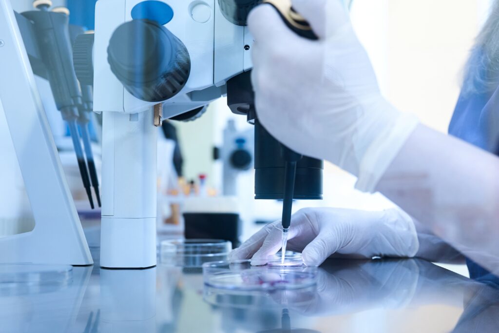 Embryologist working under a microscope in a fertility lab, using a precision pipette to handle cells in a Petri dish for assisted reproductive procedures.