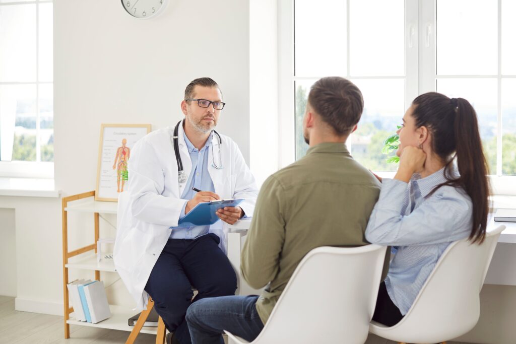 Couple meeting with a fertility specialist in a bright medical office, discussing fertility evaluations and treatment options as the doctor takes notes on a clipboard.
